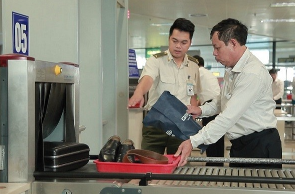 Nhân viên an ninh hàng không kiểm tra hành lý xách tay hành khách tại điểm soi chiếu